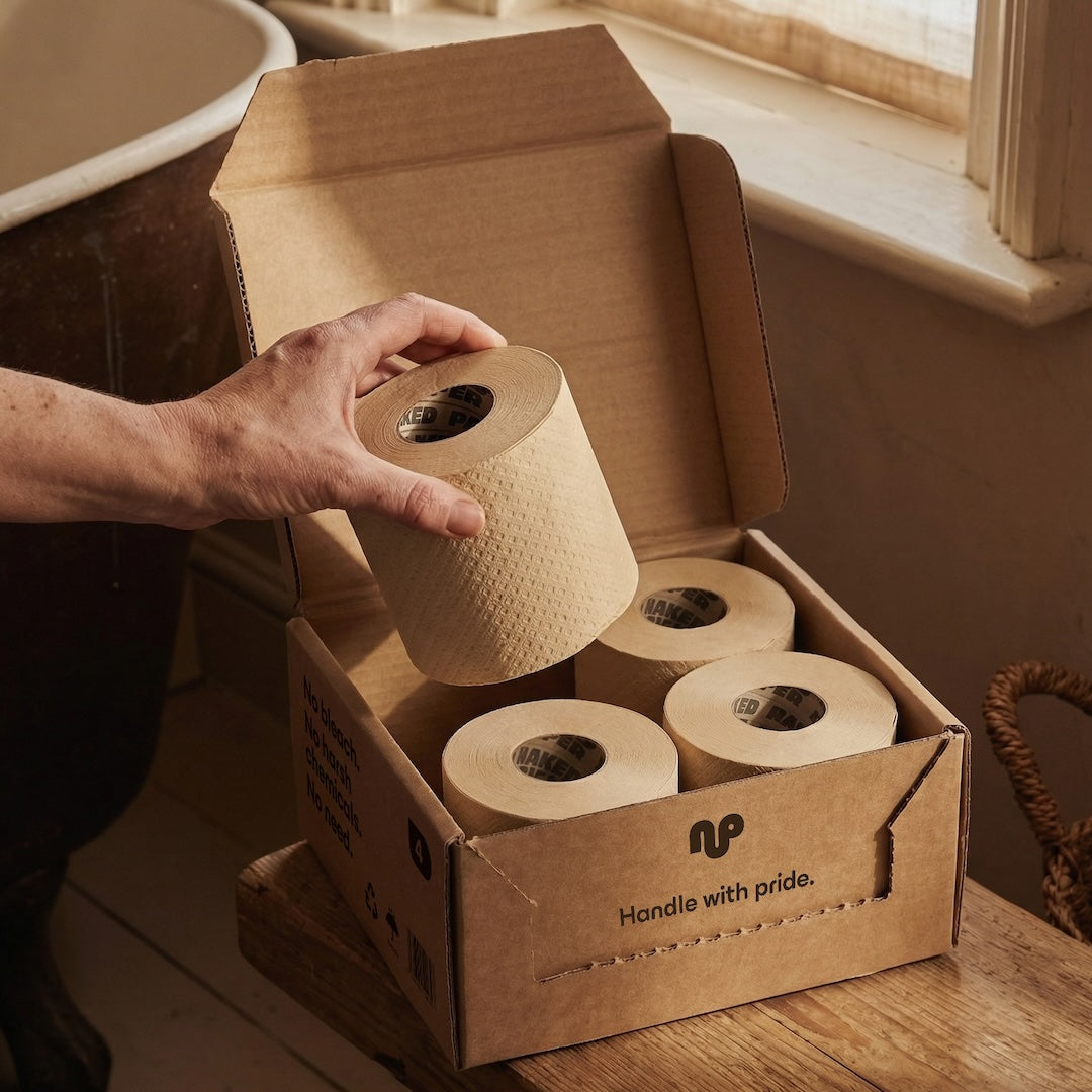 Naked Paper Trial Box opened in the bathroom, with a hand taking out a roll from the box